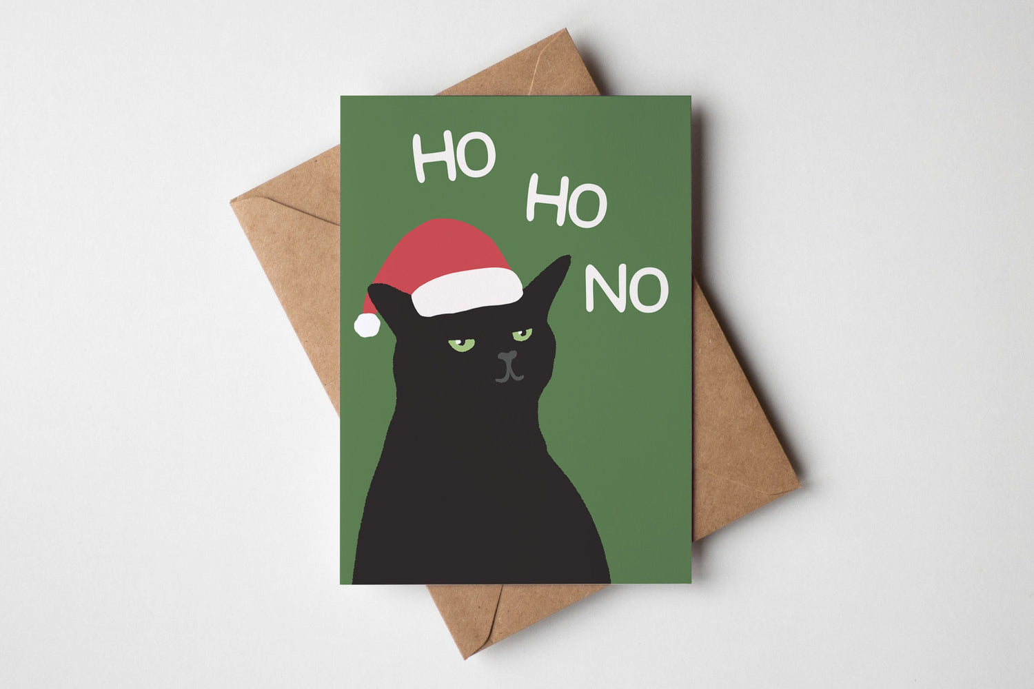 Christmas card with a black cat wearing a Santa hat and 'HO HO NO' text, placed on a brown envelope.