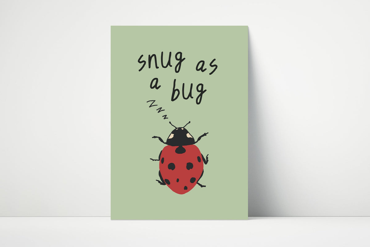 A vertical art print with a sage green background featuring the handwritten text 'snug as a bug' above a red ladybug illustration, leaning against a white wall on a white floor.