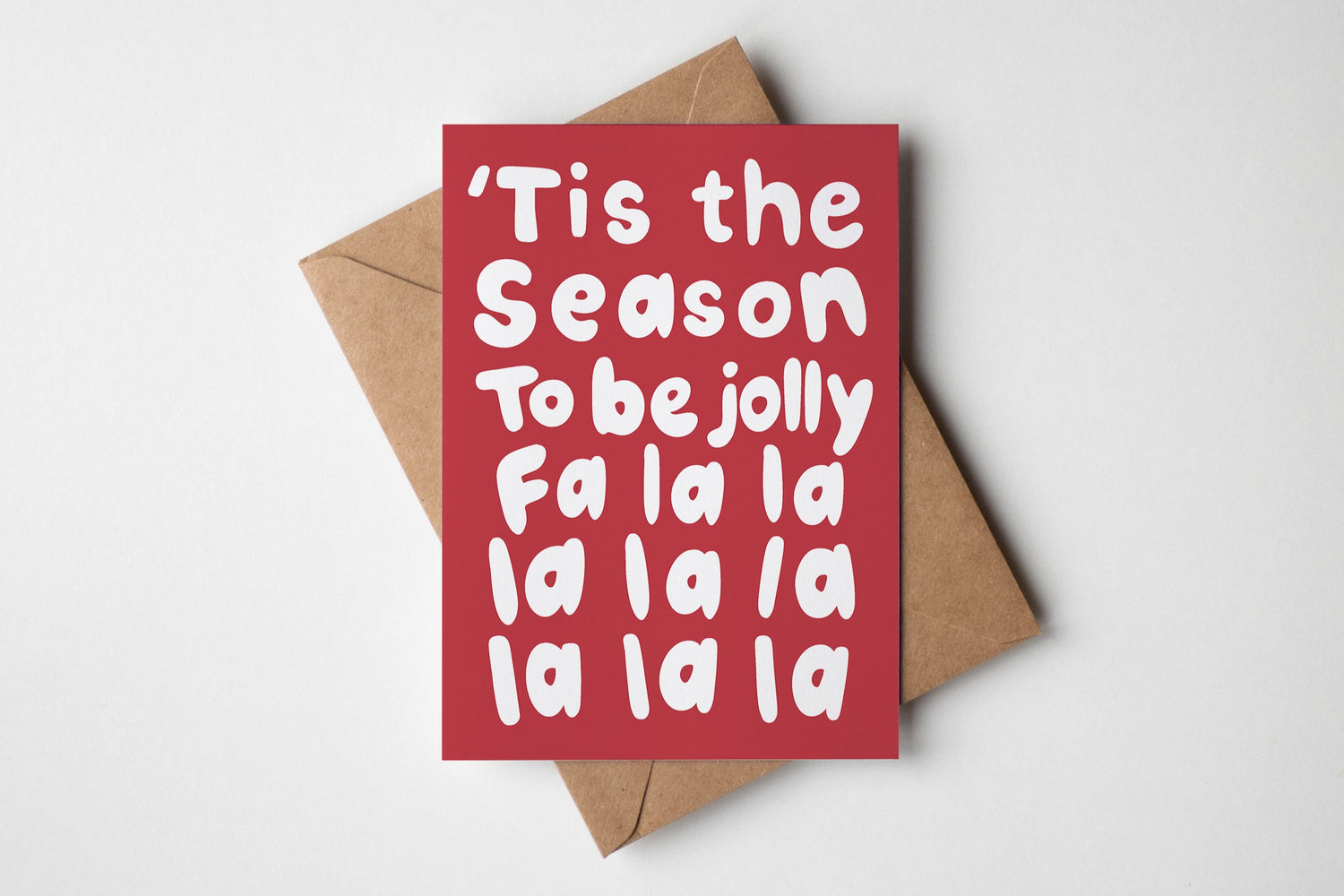 Red card with white hand lettered text 'Tis the Season To be jolly Fa la la la la la la la la'