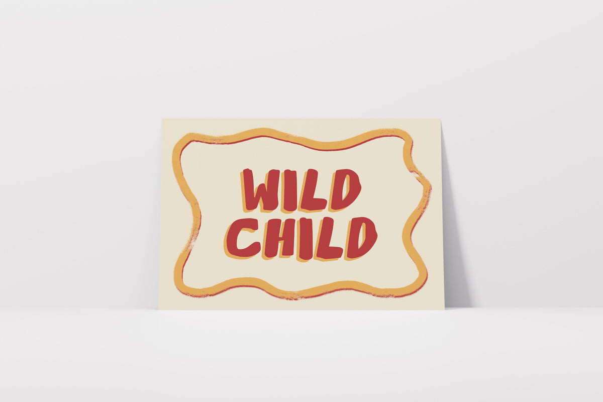 A square art print with the words 'WILD CHILD' in red bubble letters inside a wavy orange border on a cream background, leaning against a light gray wall.